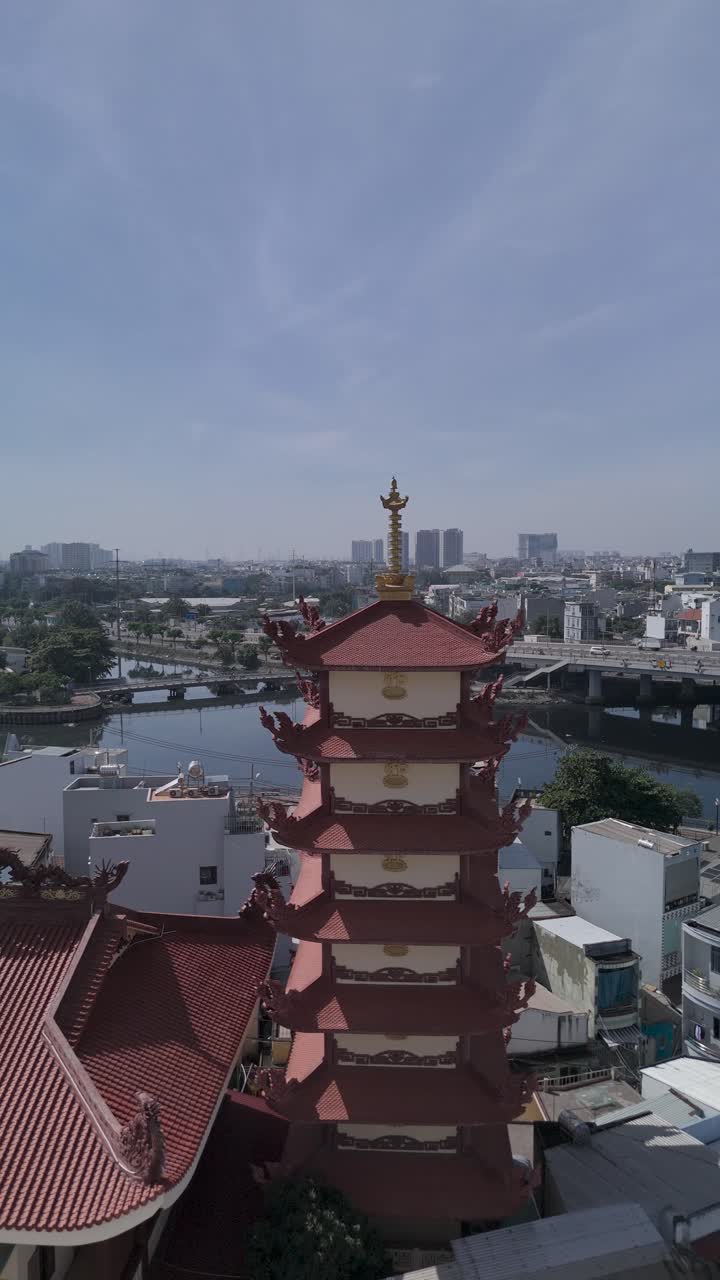 Orbit CW Vertical drone view over Buddhist pagoda in busy urban area of Ho Chi Minh City, Vietnam on a sunny clear day featuring transportation infrastructure of main roads and canals in background