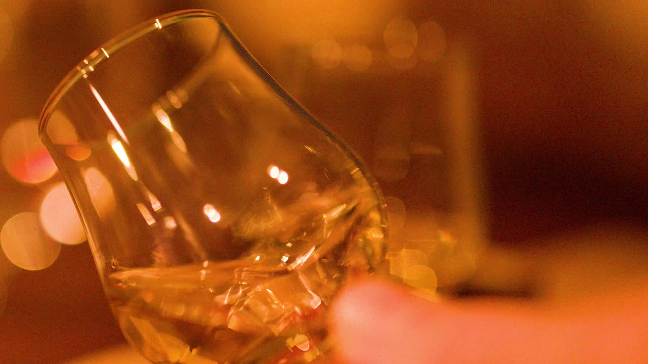 Close-up of hand gently swirling whisky glass, golden liquid, soft bokeh, warm indoor lighting