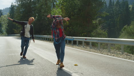 cheerful friends hitchhiking forest on highway road. smiling couple enjoy jump.