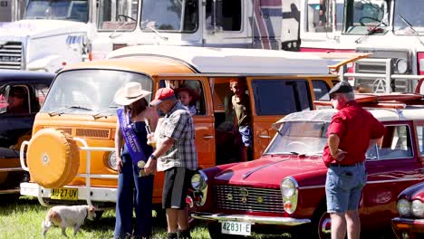 personas que interactúan cerca de coches clásicos y un concurso de belleza