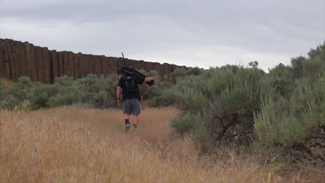 male photographer carries huge camera on tripod toward rock columns