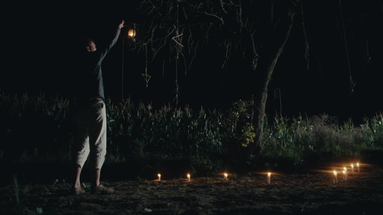 Night scene with a person, lantern, and candles in a field