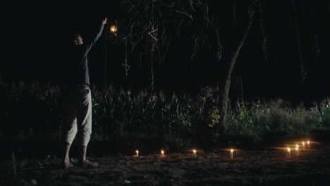 night scene with a person, lantern, and candles in a field