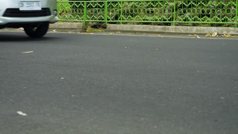 Low-Angle-Aufnahme-Einer-Balinesischen-Straße-Mit-Fahrenden-Motorrollern-Und-Autos-Durch-Die-Stadt-In-Ubud-Auf-Bali,-Indonesien.-Viel-Verkehr-Auf-Bali