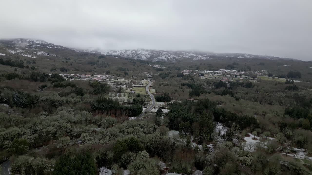 Villaggio innevato con vegetazione invernale e montagne innevate all'orizzonte sotto un cielo nuvoloso a Picornio, in Galizia
