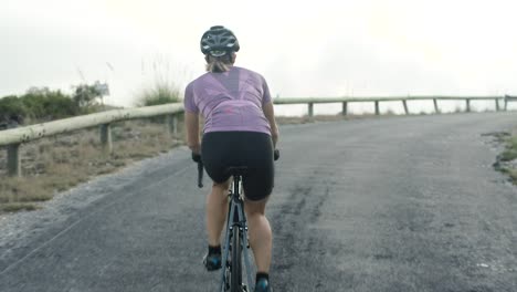 muscular build female athlete riding road bicycle on winding mountain road on a beautiful sunny summer day, view from the waist down, medium shot