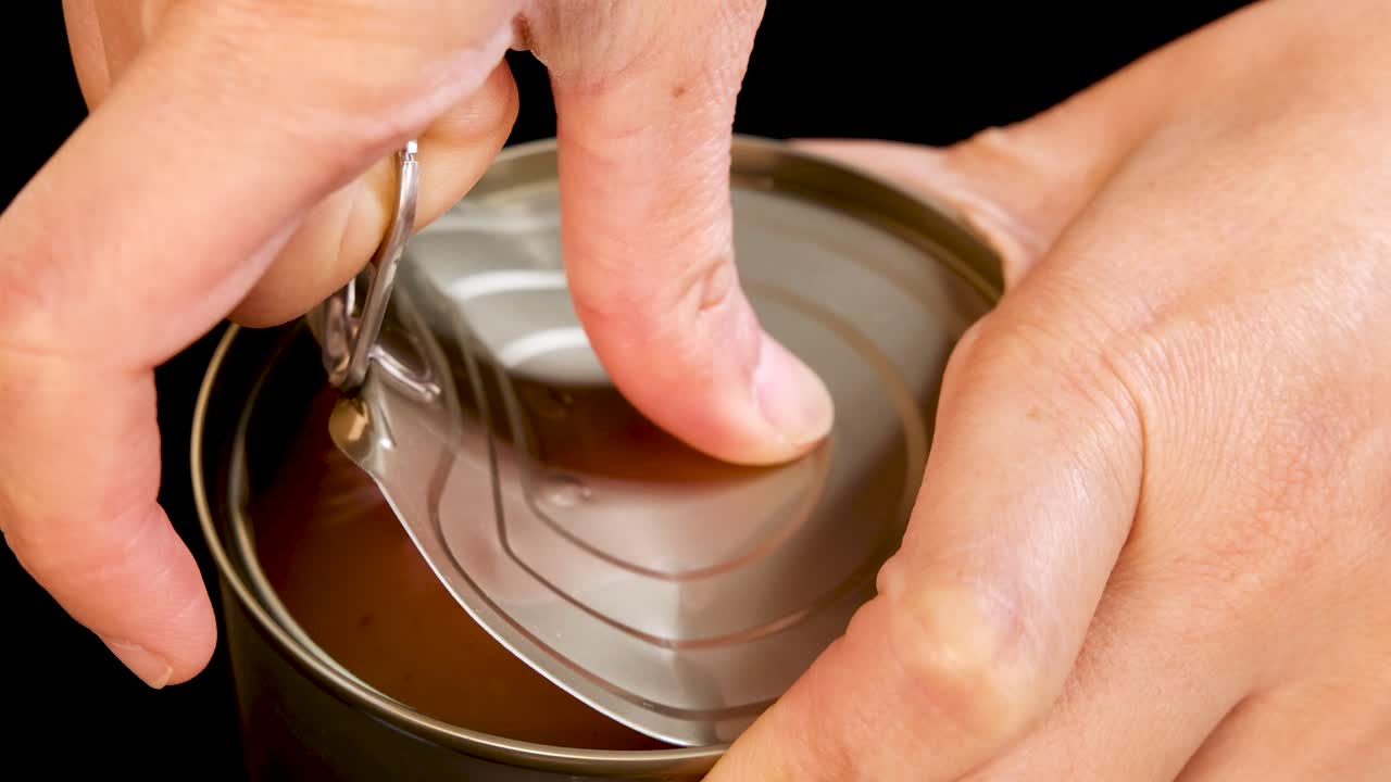 A close-up sequence shows hands opening a pull-tab can of tuna chunks in mineral water under bright, even lighting with a static camera angle