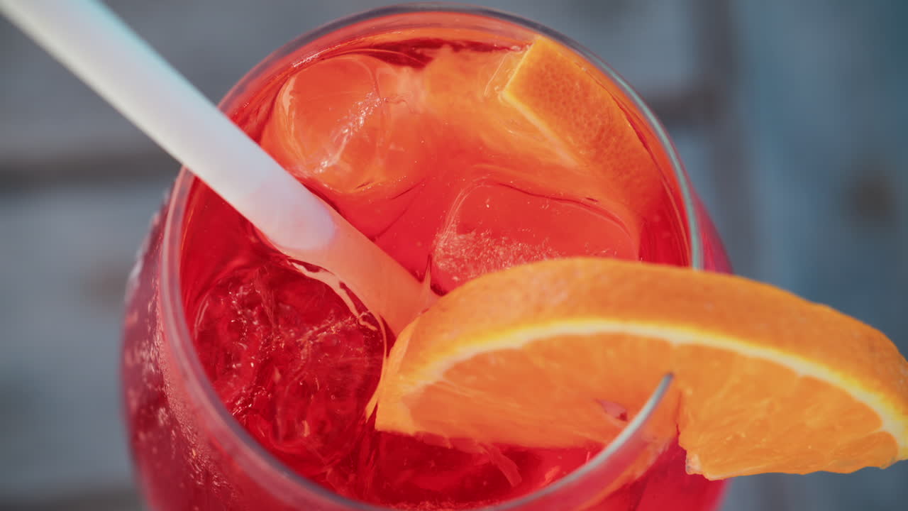 Primo piano di un cocktail rosso-arancio rinfrescante con una fetta d'arancia e cubetti di ghiaccio, scattato all'aperto in una giornata di sole a Cannes