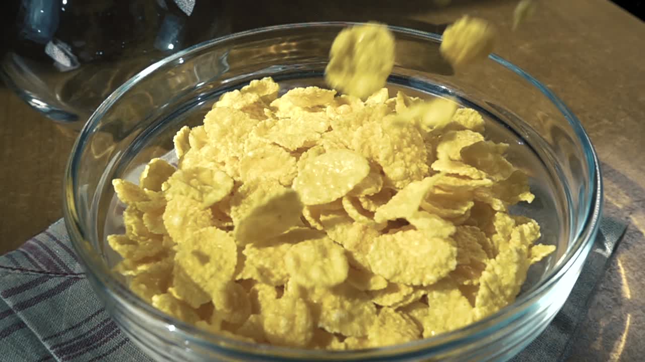 Fiocchi di mais gialli croccanti nella ciotola per una deliziosa colazione mattutina con latte. Slow motion con ripresa rotatoria.