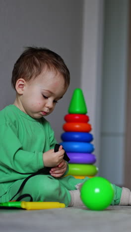 peaceful baby boy plays sitting on the floor. kid stretches the cord in his hands. toy box and toys are scattered around. vertical video