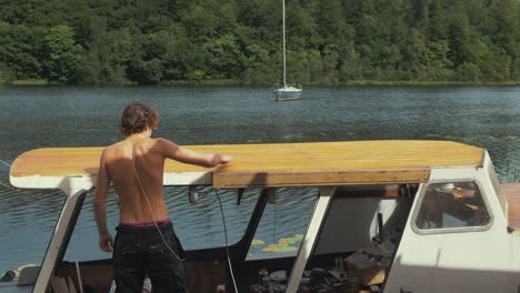 youth topless wipes down sanded roof of wooden boat before varnishing