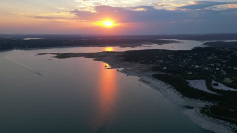 a boat speeding across lake travis as a fiery sunset is reflected on the water