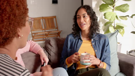 chatting and relaxing, female friends enjoying coffee together on cozy living room sofa