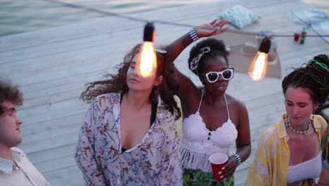 positive diverse friends dancing with drinks at lake party