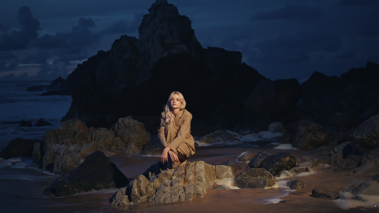 mujer sentada en la playa de la noche en las rocas. modelo de moda posando en la costa oscura del océano