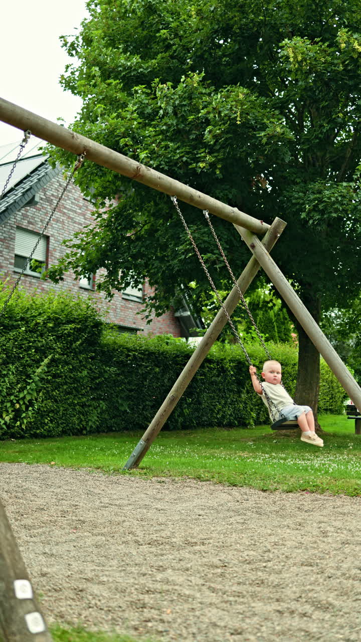 Giovane madre a passeggio al parco giochi con il suo figlio piccolo. Madre europea felice e sorridente che dondola con il suo figlioletto su un'altalena nel parco. Concetto di gioco e momenti felici.