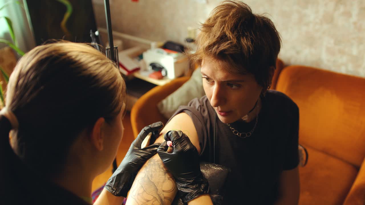 Young Woman Having Talk with Tattoo Artist Applying Ink to Her Skin