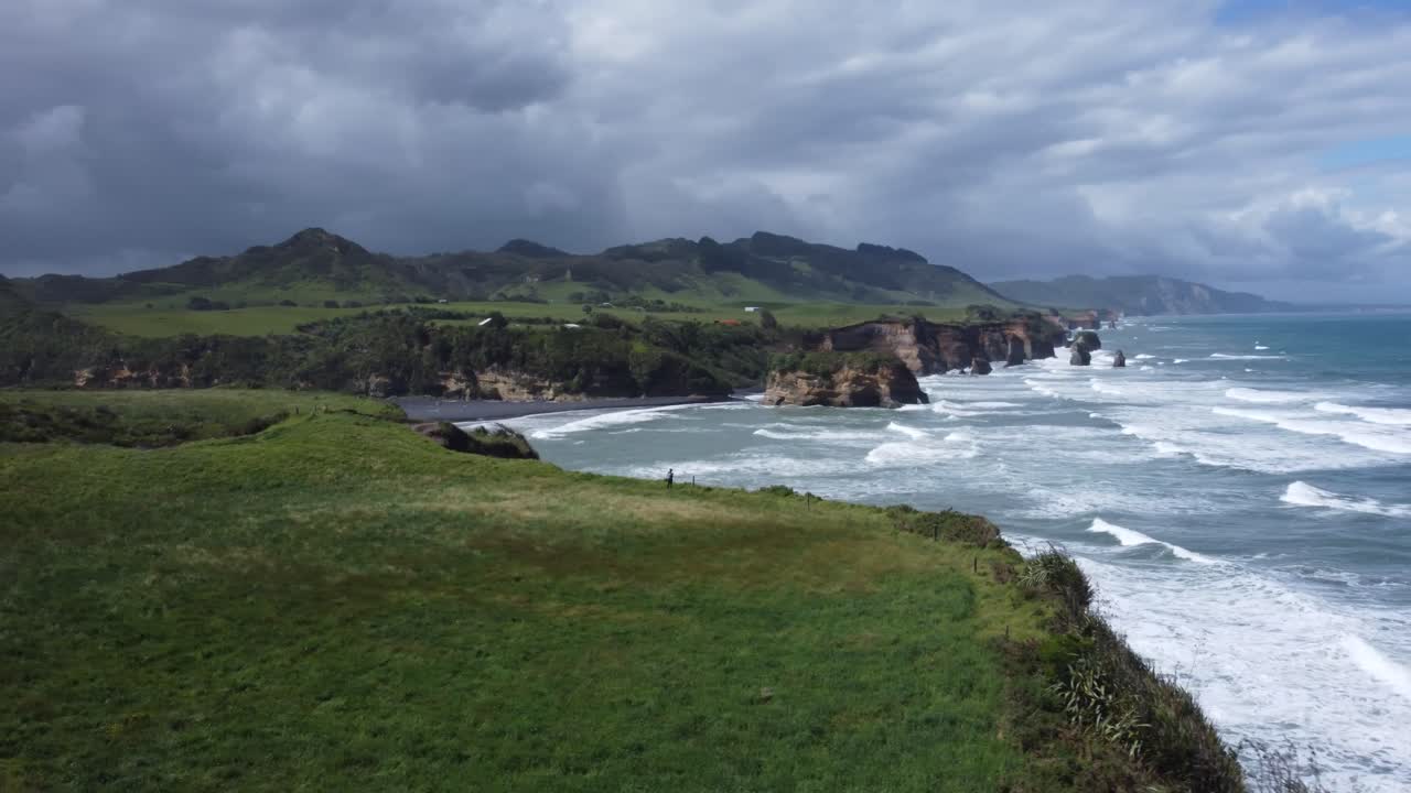 Drone view of a person standing on a cliff and the coast, rocks and ocean on a sunny summer day at Three Sisters and Elephant Rock, New Zealand.