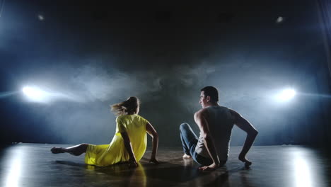 a man and a woman dance together a funny dance in jeans and a yellow dress on stage in smoke. musical.