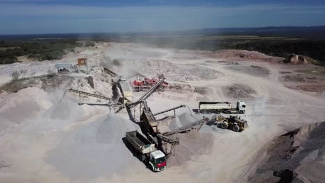 Vista-Aérea-De-Una-Cantera-De-Piedra-En-Funcionamiento-Con-Trituradoras-De-Piedra,-Bulldozers,-Camiones-En-Un-Entorno-Natural-Con-Luz-Natural