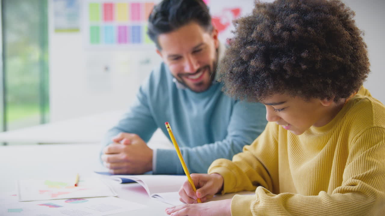 maestro masculino con estudiante masculino en el aula de la escuela sentado en el escritorio escribiendo en el libro juntos