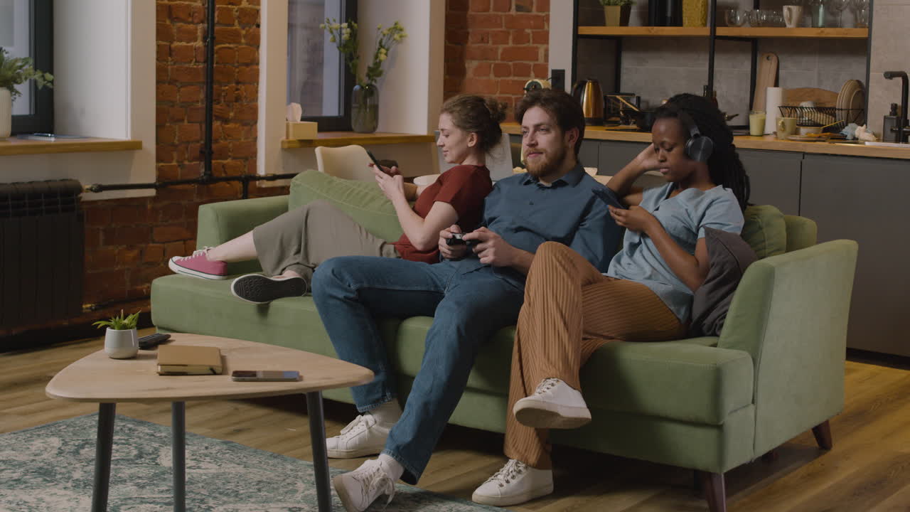 스마트폰을 사용하는 세 명의 롬메이트, 비디오 게임, 집에서 소파에 앉아 스마트폰으로 음악 듣기 1
