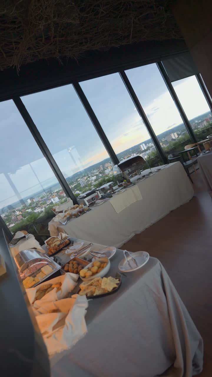 Una mesa de bufé con una variedad de alimentos y una vista del horizonte de la ciudad. La escena es relajada y acogedora, ya que la comida está dispuesta de forma atractiva.