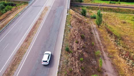drone is flying over the road with a luxury car moving along the highway. beautiful white audi driving on the bridge. aerial view.