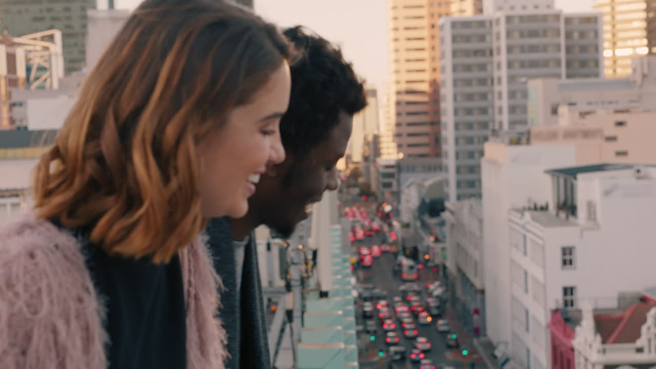 행복한 다민족 커플이 웃고 즐겁게 옥상에서 도시의 전망을 즐기고 채팅하고 연결을 공유하고 친구들이 술을 마시고 주말에 놀고 있습니다.