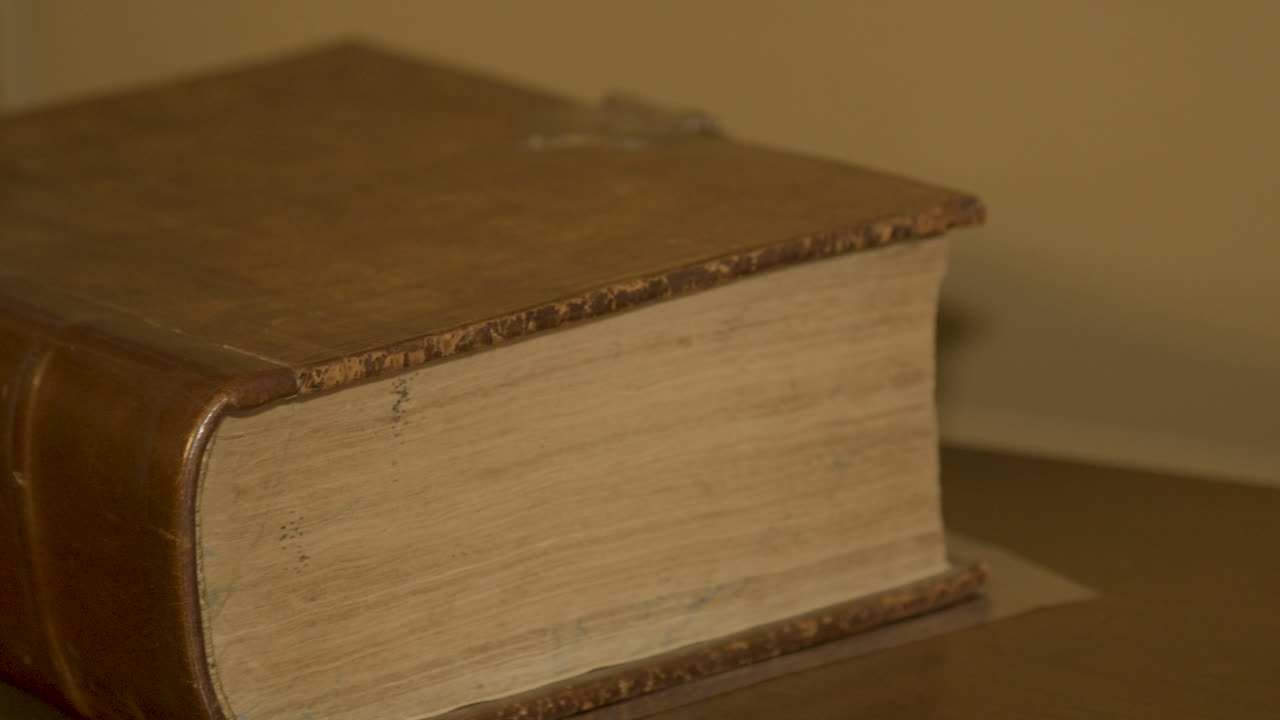 Крупный план с панорамированием мимо большой старой книги, лежащей на антикварном столе.