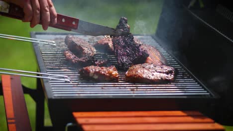 man flipping barbecued ribs on coal grill in his garden