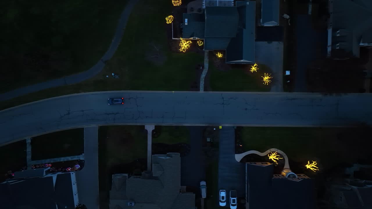 Top down shot of car traveling through gated neighborhood with large homes decorated for Christmas