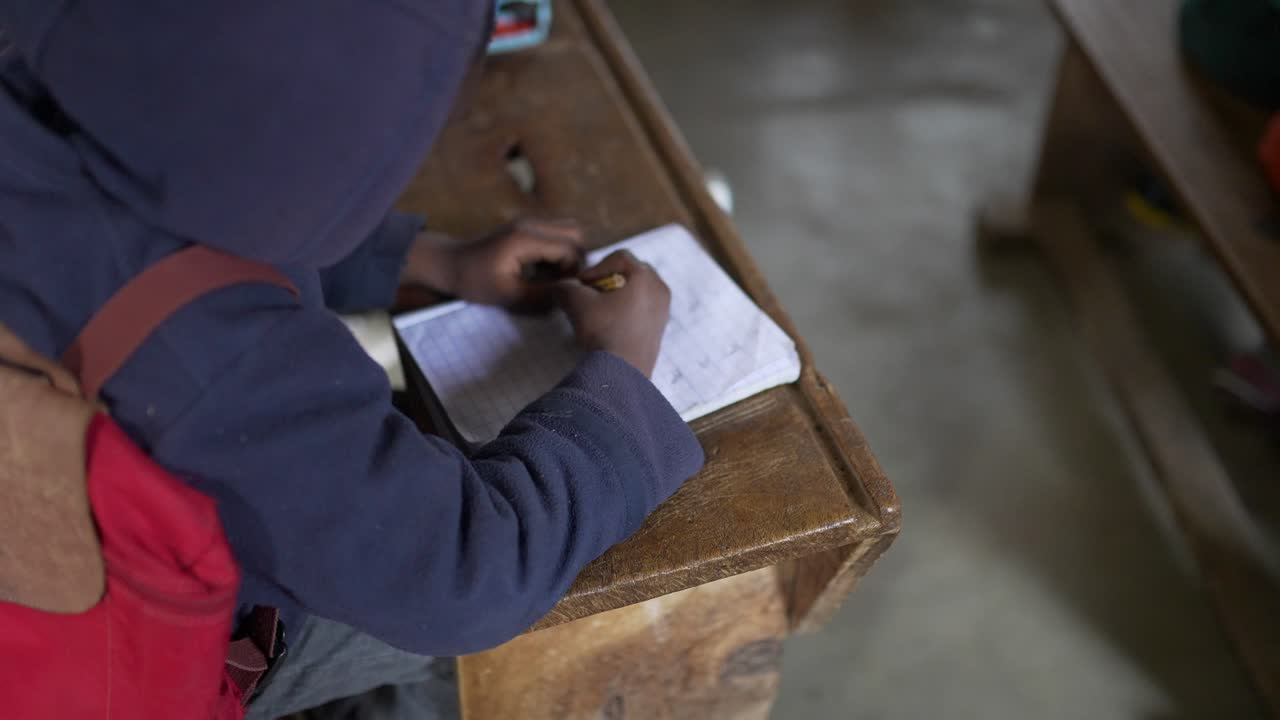 Black poor African kid doing homework, writing in his notebook at school