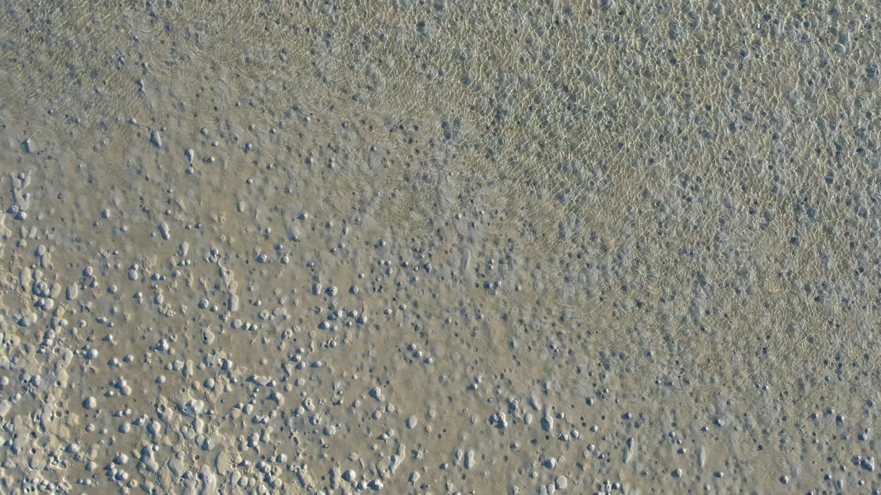 tomada de un avión no tripulado de una llanura de marea con agua azul clara y agujeros en la arena, ángulo hacia abajo aérea costera