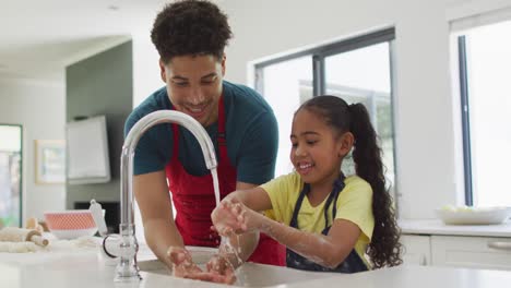 Happy-biracial-father-and-daughter-washing-hands-in-kitchen