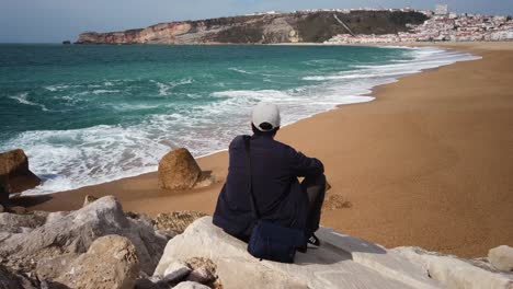 young man sitting on a rock watching breaking waves