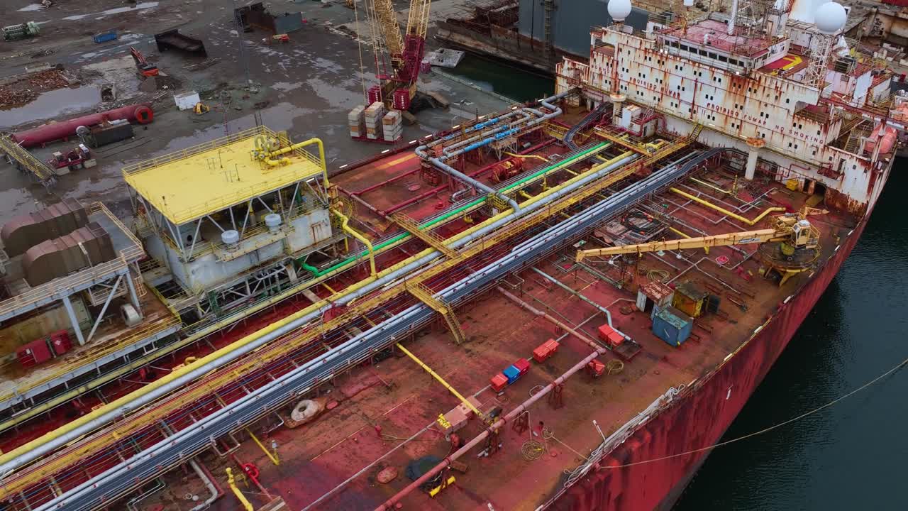 Aerial drone footage of a red tanker ship featuring a rust-covered deck with old equipment and a corroded superstructure. Industrial maritime decay captured from above.
