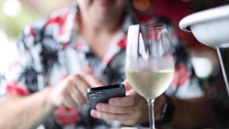 close-up of a man texting with wine in foreground