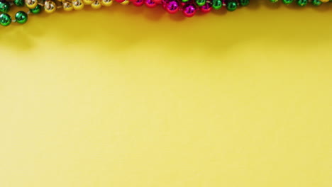 video of pink, gold and green mardi gras carnival beads on yellow background with copy space