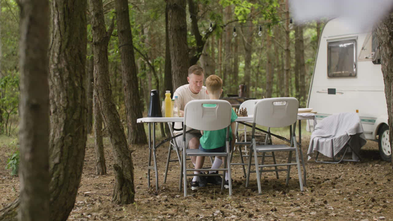 padre e hijo jugando al ajedrez sentados a la mesa en el campamento en el bosque