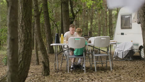 father and son playing chess while sitting at table at the camping in the forest