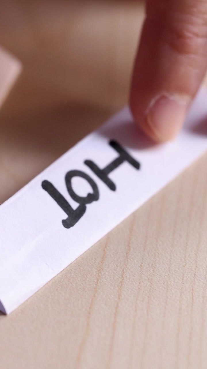 Close-up of hand using black marker to write 'Hot' on white paper strip, natural lighting