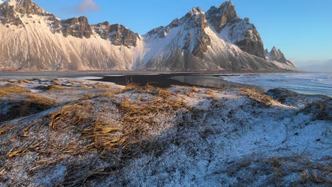 vestrahorn mountain en islandia, dolly forward wilderness paisaje invernal de tierras nevadas de la costa, montaña rocosa y costa en segundo plano.
