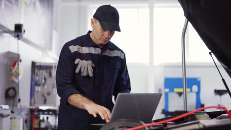 portrait of mechanic uses a laptop while conducting diagnostics test on engine, slow motion