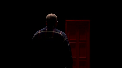 man facing a red door in the dark