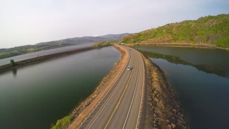 Una-Toma-Aérea-De-Automóviles-En-Una-Carretera-Cruzando-Un-Lago-O-Embalse.