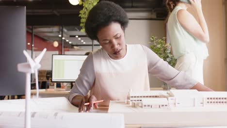 Happy african american female architect inspecting architectural model at work, in slow motion