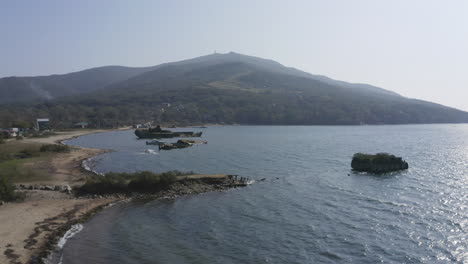 open shot of beach coastline with derelict partially submerged shipwreck aground near the shore