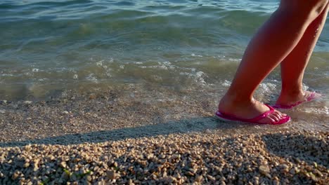 Person-walking-on-the-beach-at-sunset-during-summer-vacation-holidays-slow-motion,-closeup-of-legs-and-feet-in-the-sea-water,-4k-video