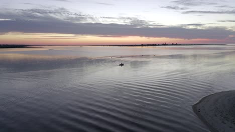 Asombrosa-Puesta-De-Sol-Sobre-El-Océano-Y-Un-Hombre-Solitario-Remando-Hacia-El-Mar-En-Un-Bote-Pequeño-Mientras-El-Cielo-Está-En-Llamas-Desde-La-Puesta-De-Sol